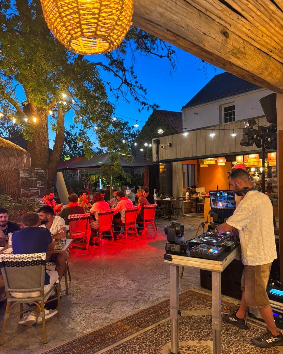 des convives profitent de la terrasse illuminée pendant que le DJ met l'ambiance sur le côté